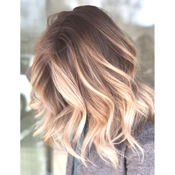 Donna con capelli mossi, radici castane che sfumano verso le punte bionde.