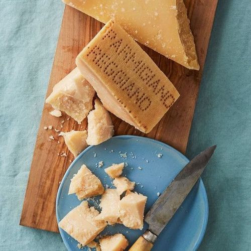 Formaggio Parmigiano Reggiano su un tagliere di legno con un coltello e un piatto blu.