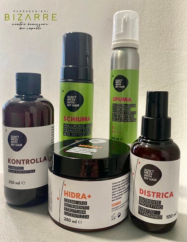 Cinque prodotti per la cura dei capelli con etichette nere e dettagli verdi, tra cui shampoo, schiuma e creme per lo styling.