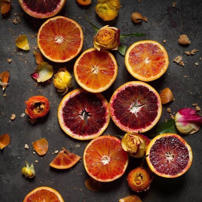 Fette di arance rosse con fiori gialli e arancioni su una superficie scura.