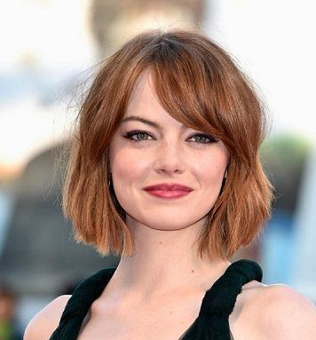 Donna con capelli corti, biondo-rossicci e frangia laterale, che indossa un top verde scuro e sorride.