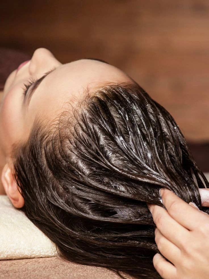 Persona che riceve un trattamento per capelli; mani che massaggiano l'olio sui capelli bagnati.