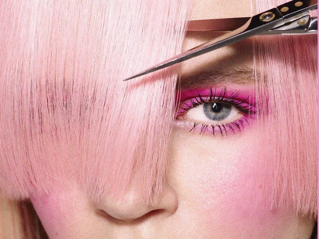 Donna con i capelli rosa e il trucco che viene rifinito con le forbici.