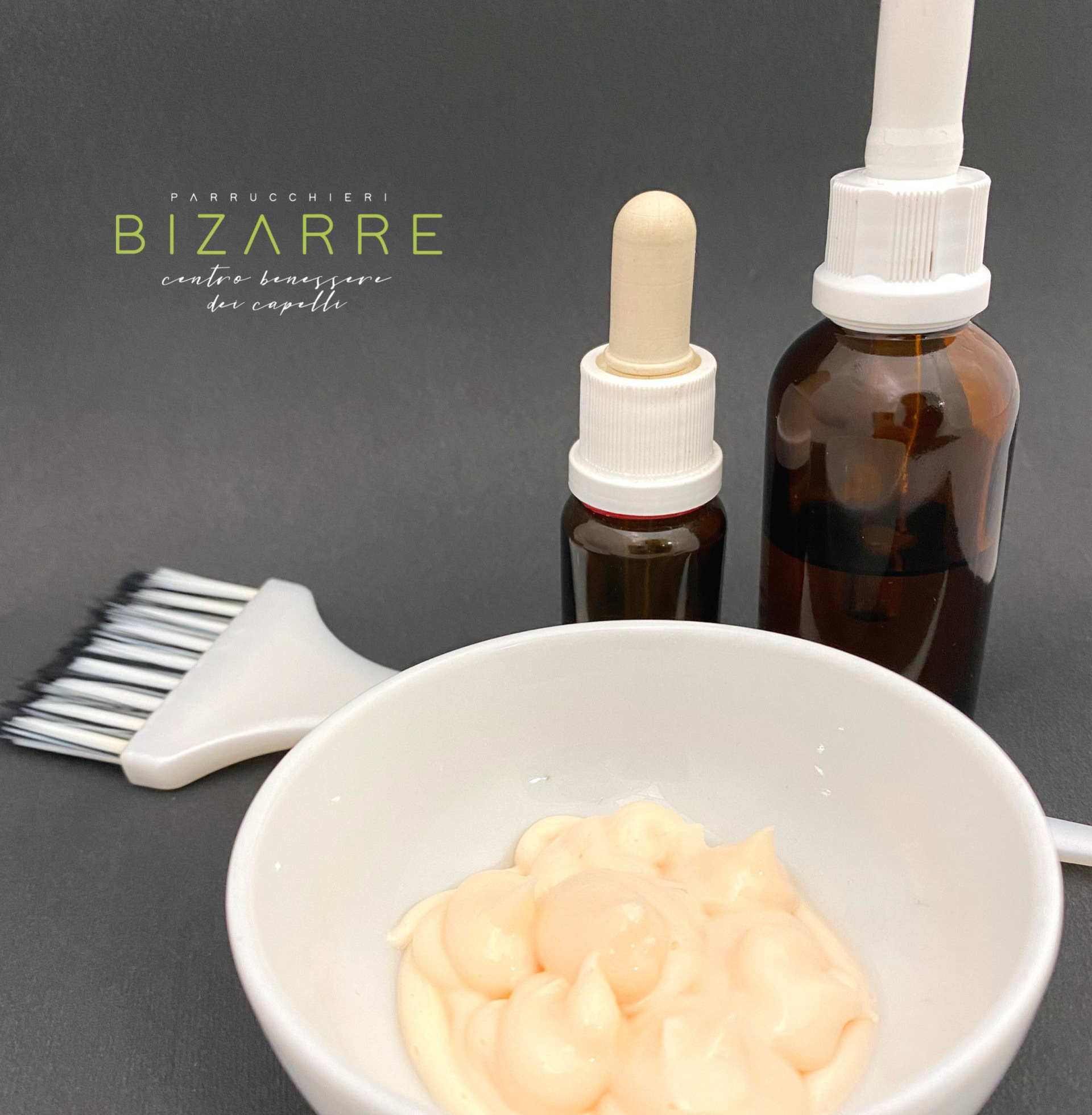 Kit per la tintura dei capelli: ciotola con crema, pennello e flaconi contagocce, posizionata su una superficie scura.