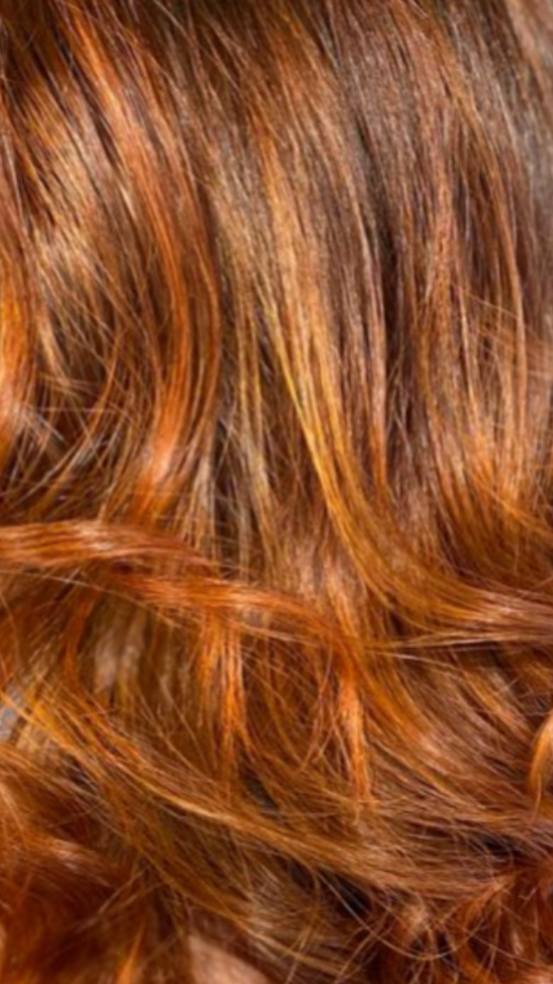 Primo piano di capelli ondulati, castano-rossicci, con riflessi ramati più chiari.