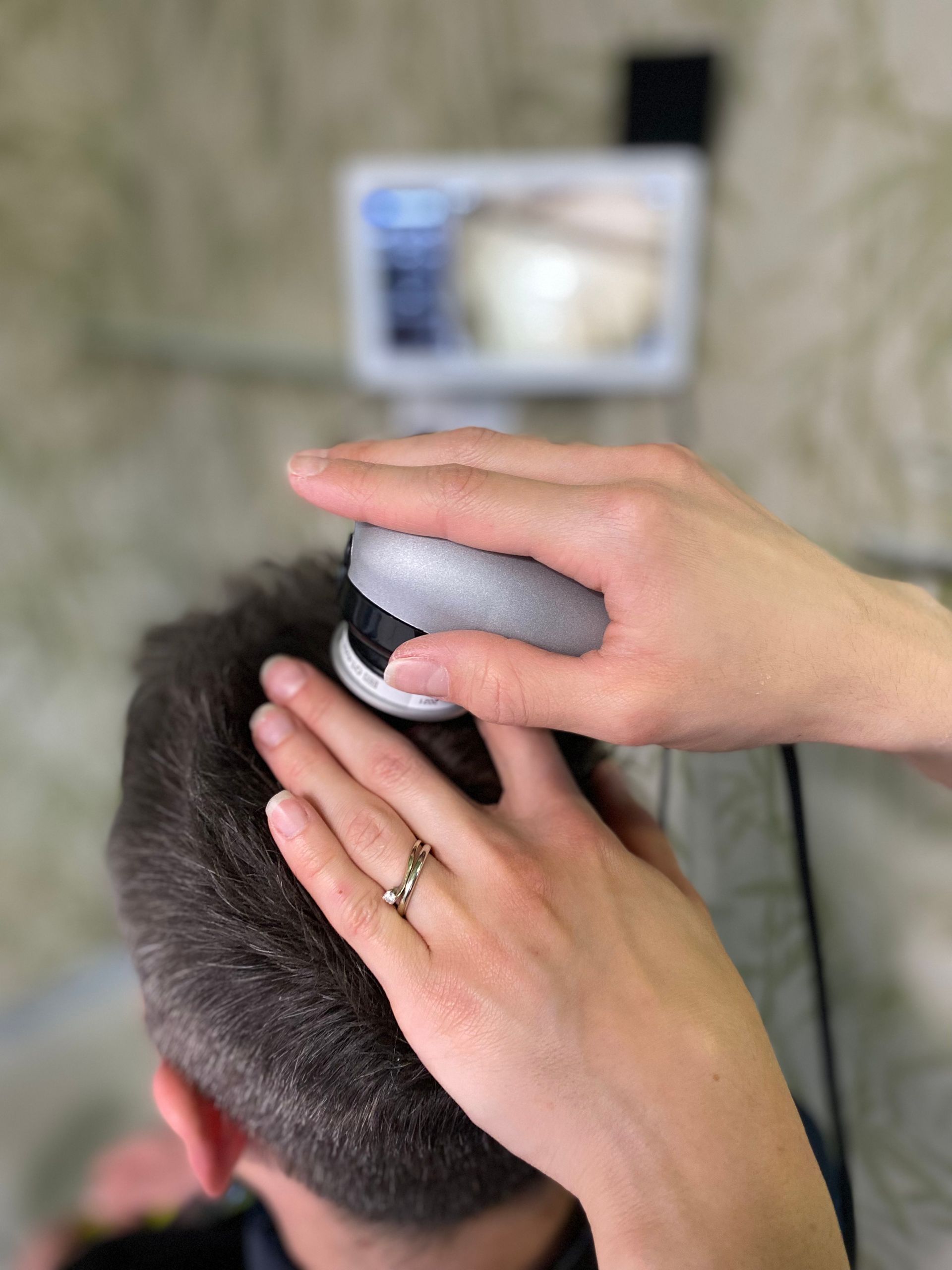 Testa di una persona esaminata con un dispositivo per l'analisi dei capelli; monitor sullo sfondo.