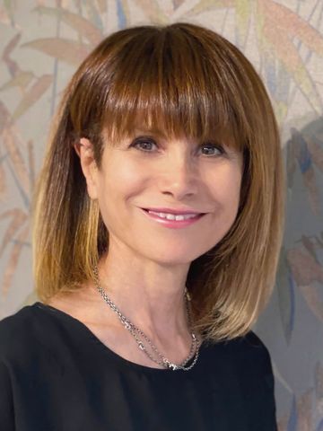 Donna con capelli castani e frangia sorride, indossa un top nero e una collana d'argento.