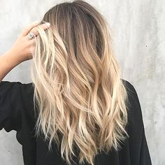 Capelli biondi ondulati di una donna con radici scure, su sfondo grigio.