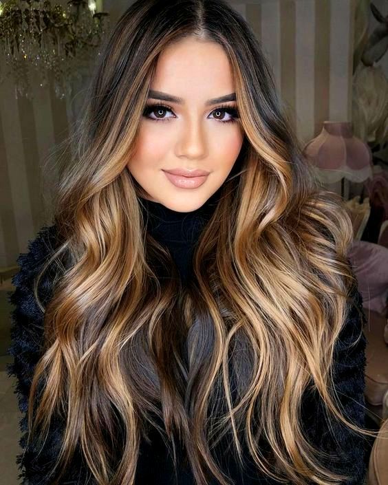Donna con lunghi capelli ondulati nelle tonalità del castano e del biondo, che indossa un top nero e sorride.