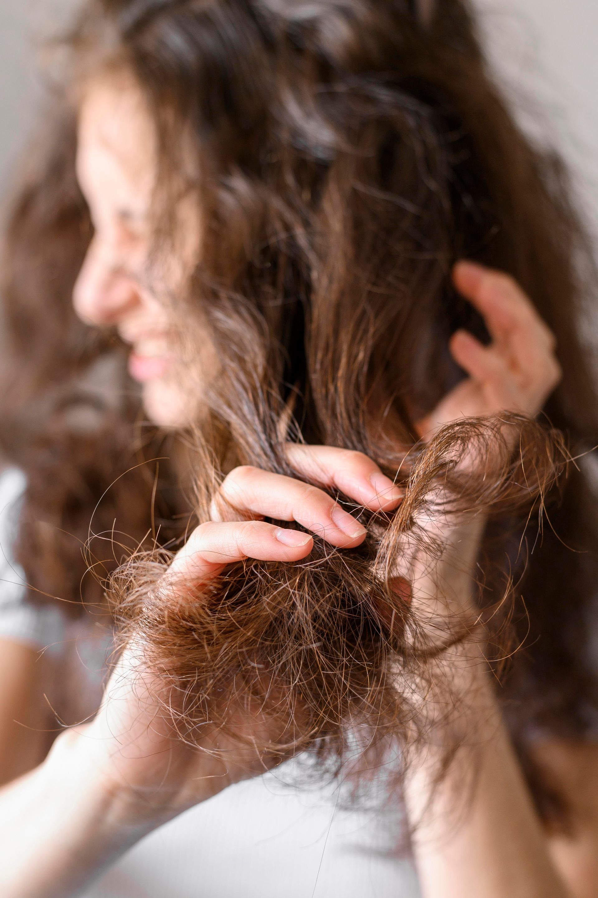 Donna che esamina i capelli castani danneggiati con espressione preoccupata.