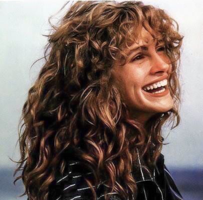 Donna con lunghi capelli castani ricci, che sorride ampiamente.