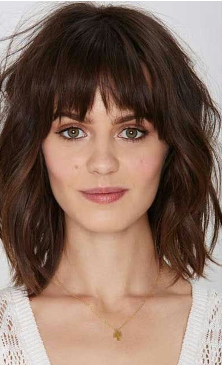 Donna con capelli castani scuri, mossi e lunghi fino alle spalle, con frangia, sorridente, che indossa una collana.