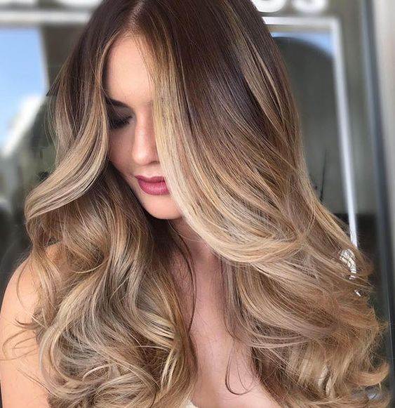 Donna con capelli lunghi, ondulati, in stile ombré, nelle tonalità del castano e del biondo, dall'espressione neutra.