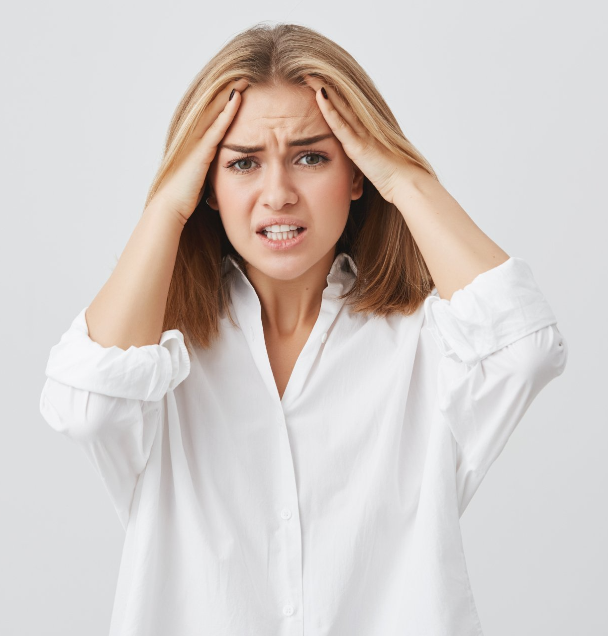 Donna dai capelli biondi, che indossa una camicia bianca, si tiene la testa con un'espressione stressata.
