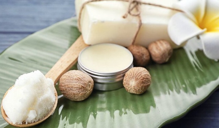 Prodotti a base di burro di karité esposti su una foglia di banano: sapone, balsamo, noci, un cucchiaio di burro e un fiore.