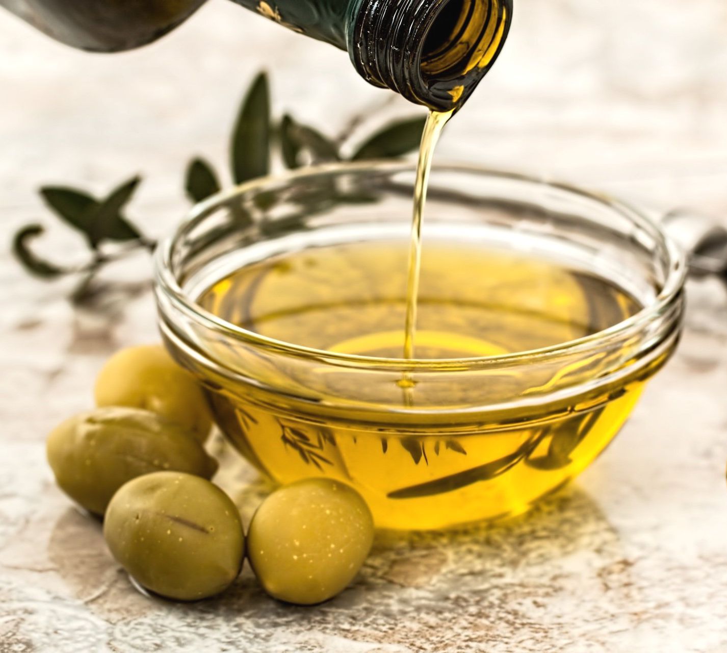 Olio d'oliva versato da una bottiglia in una ciotola di vetro, insieme alle olive.
