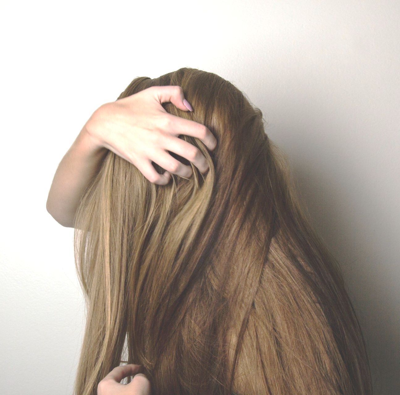 Mano che tocca lunghi capelli castano chiaro, su sfondo bianco.