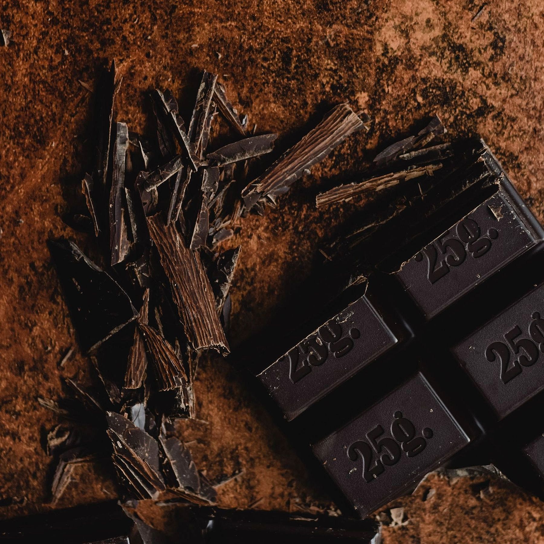 Tavoletta di cioccolato fondente con scaglie su una superficie marrone testurizzata.