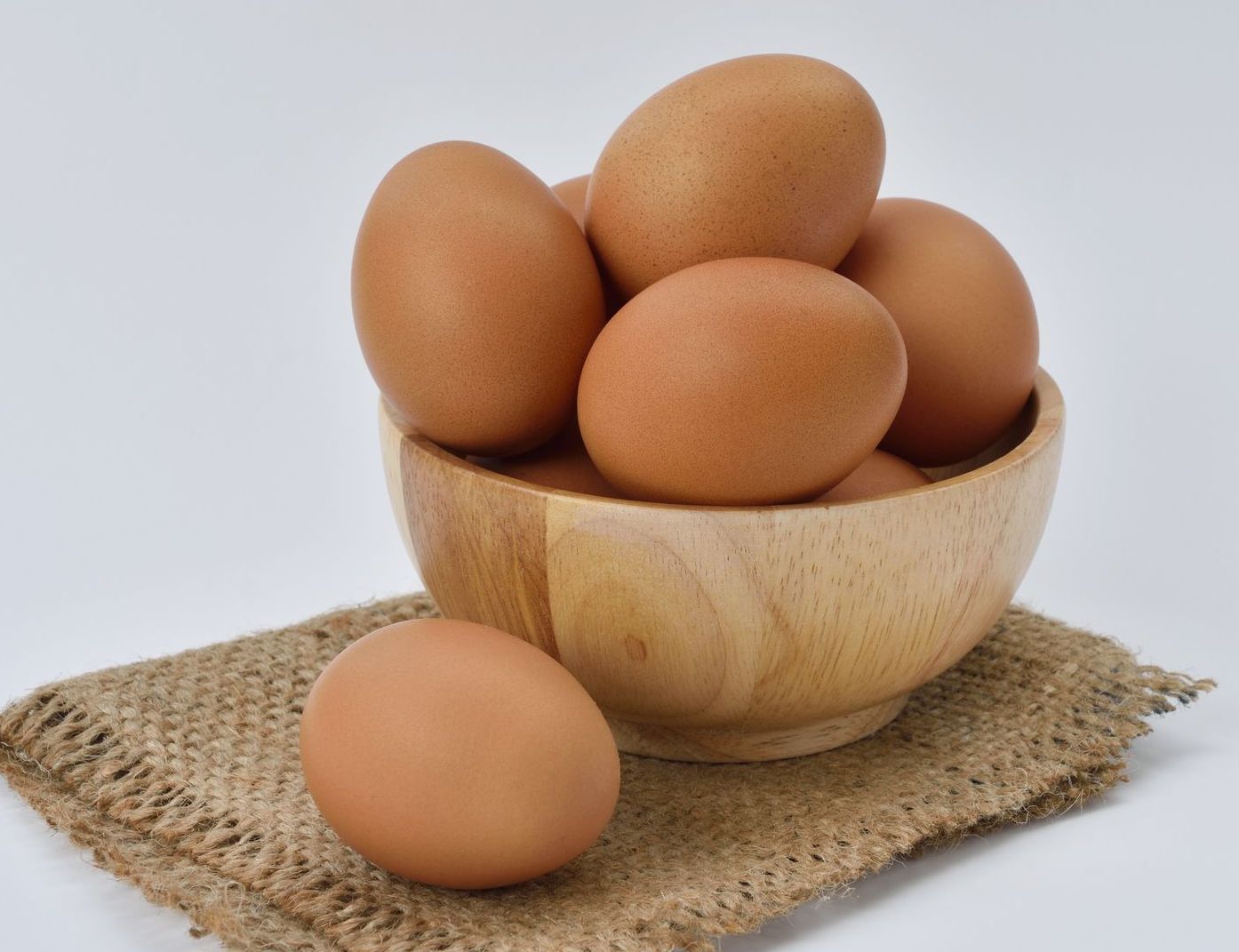 Uova marroni in una ciotola di legno su una tela di iuta, su uno sfondo bianco.
