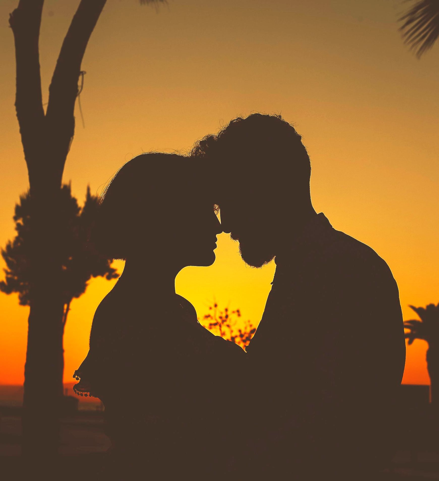Silhouette di una coppia abbracciata, teste vicine, sullo sfondo di un tramonto arancione.