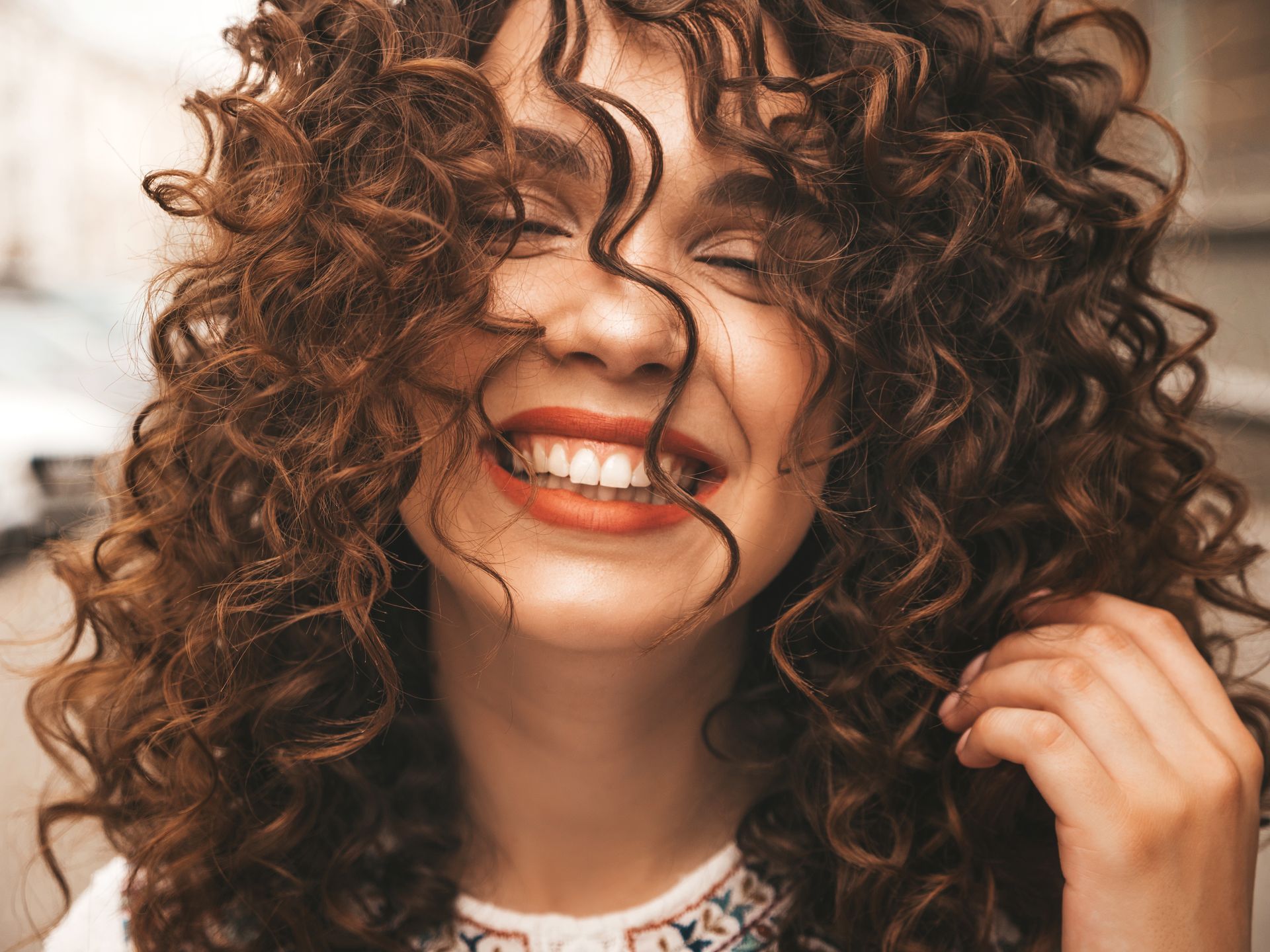 Donna con i capelli castani ricci che sorride con gli occhi chiusi.