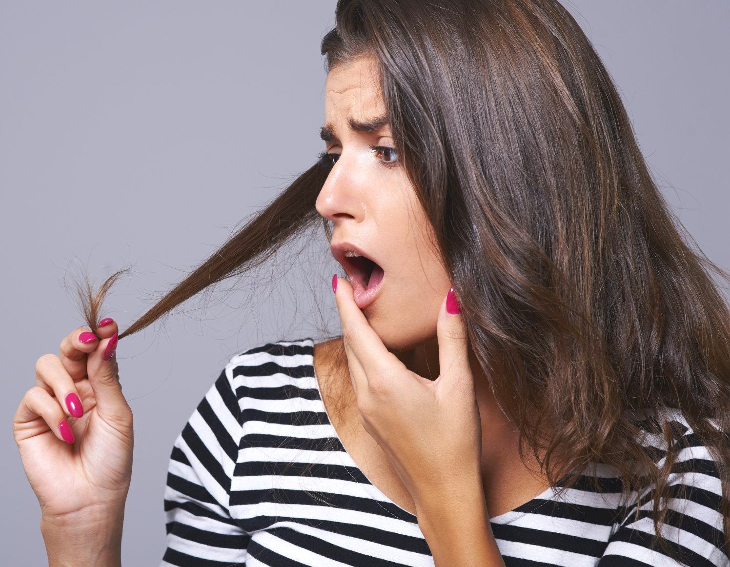 Donna con espressione scioccata, che esamina le doppie punte dei suoi capelli.