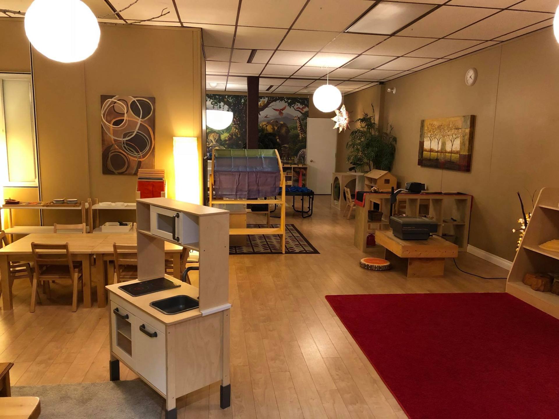 A large room with tables , chairs , a kitchen and a red rug.