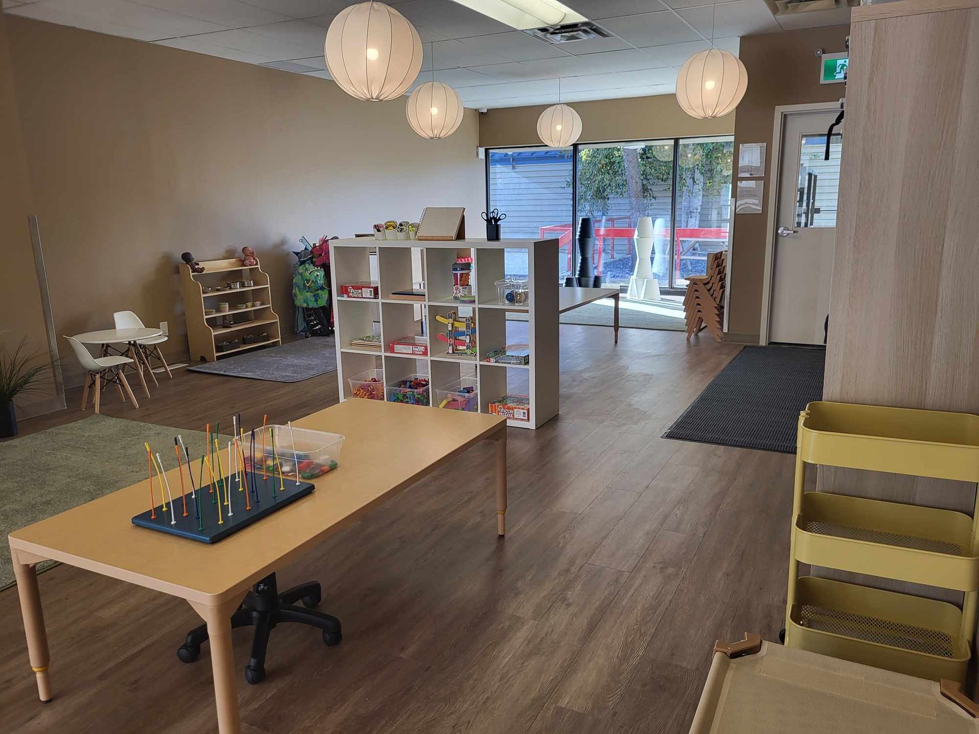 A large room with a table , shelves , chairs , and toys.