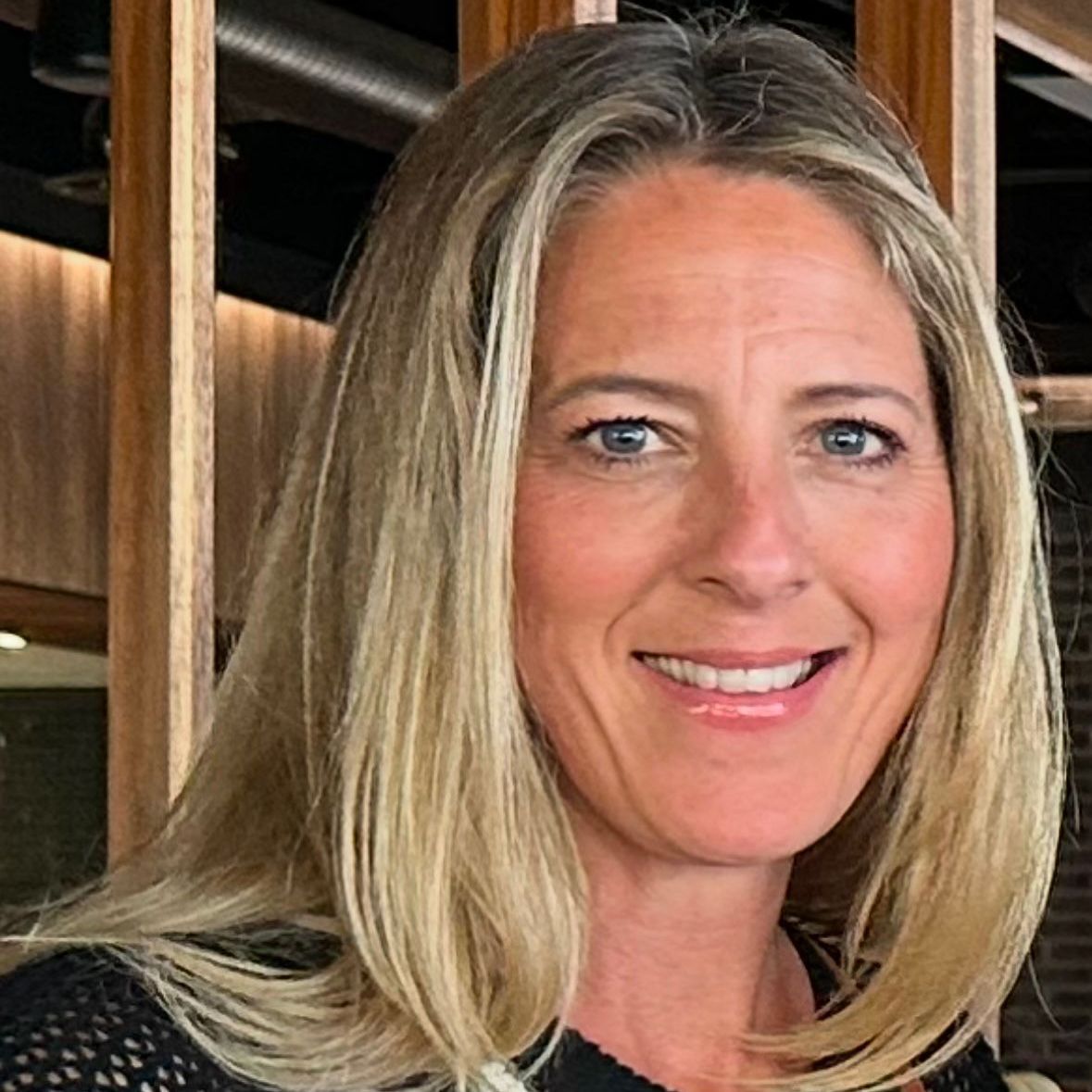 A woman with blonde hair and blue eyes is smiling for the camera.