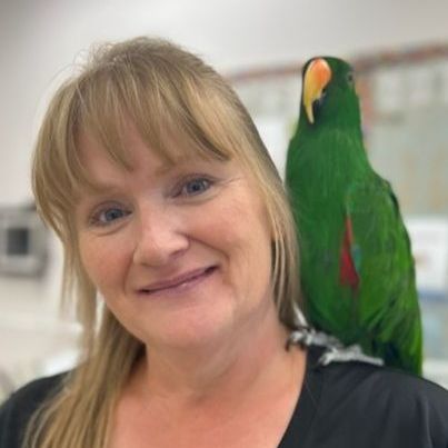 A woman is holding a green parrot on her shoulder.