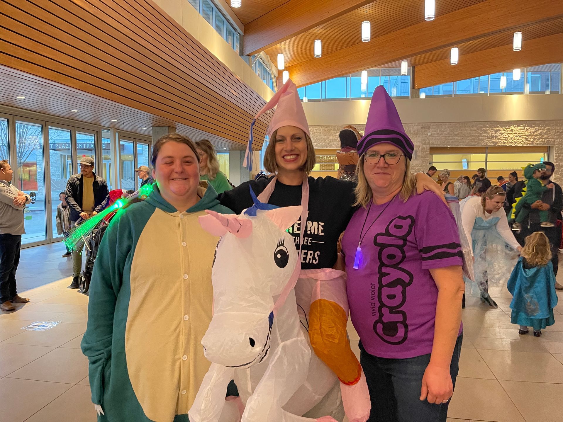 Three women are posing for a picture with a stuffed unicorn.