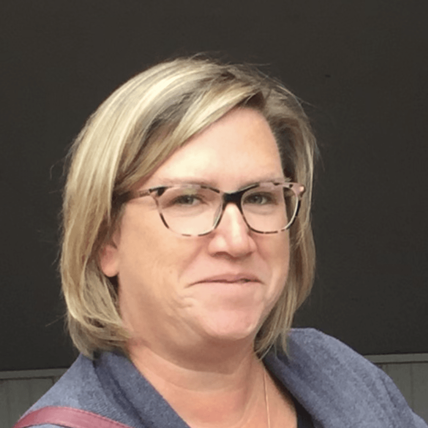 A woman wearing glasses and a blue sweater is smiling