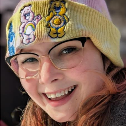 A woman wearing glasses and a beanie with care bears on it