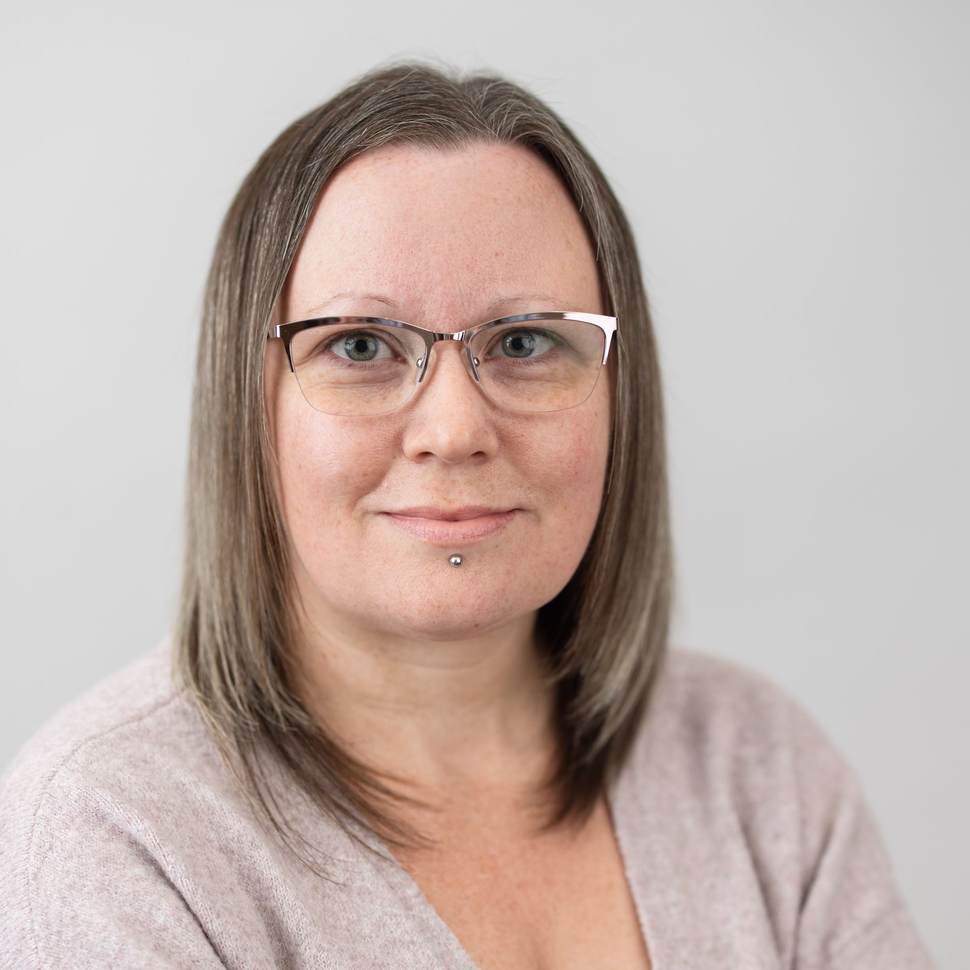 A woman wearing glasses and a pink sweater is smiling for the camera.