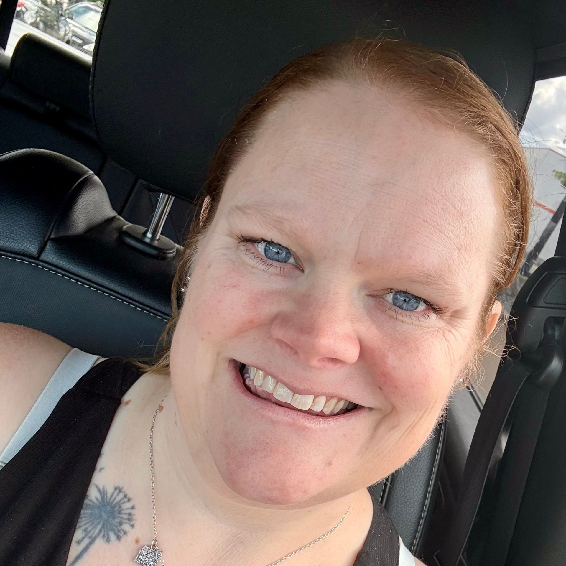 A woman with green hair and glasses is sitting in a car.