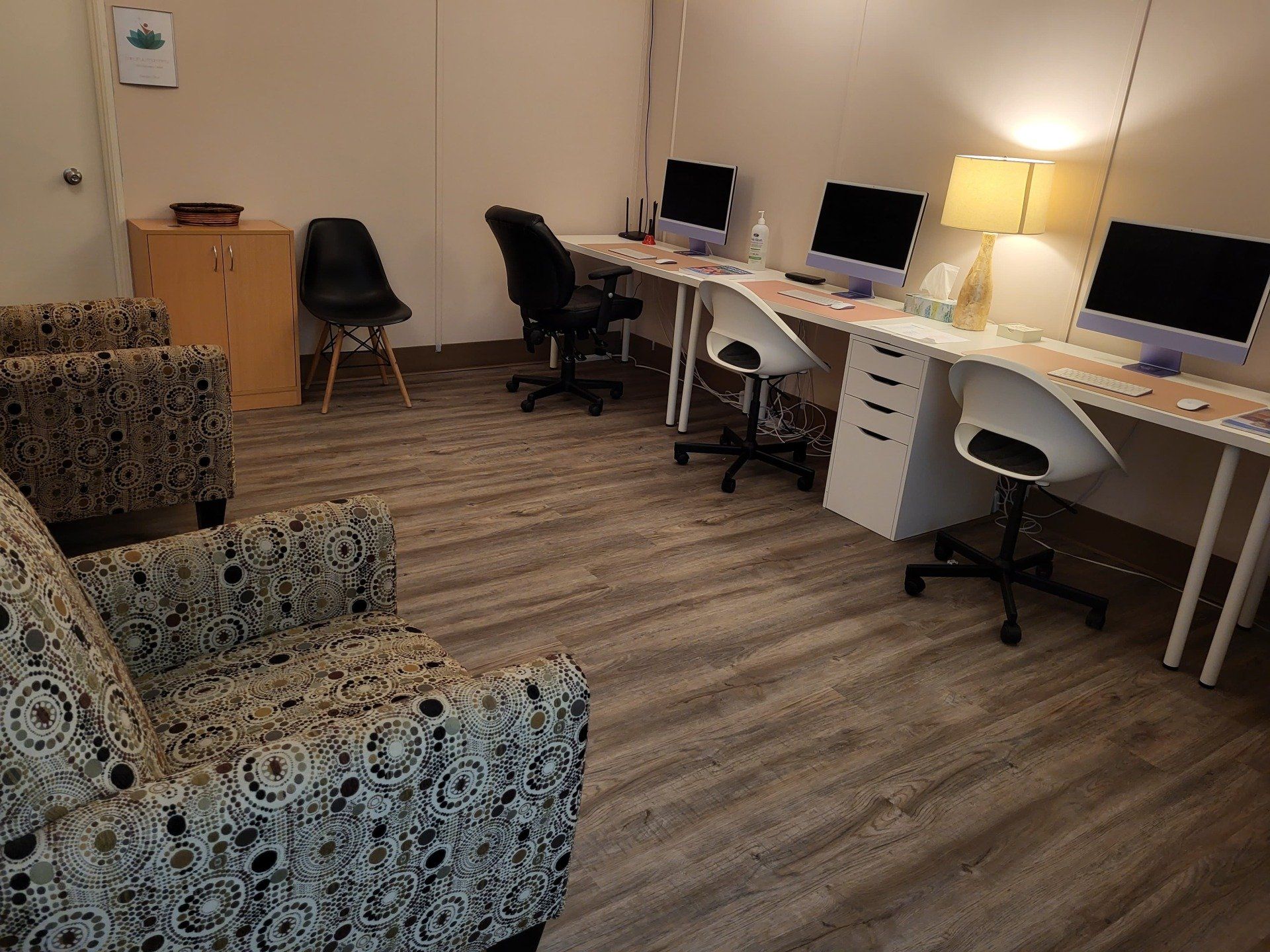 A room with a couch and chairs and computers on the desks