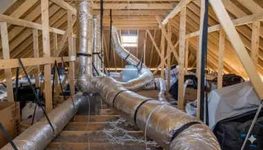 Unfinished attic showing wooden roof rafters and silver insulated HVAC ductwork running across the floor joists.