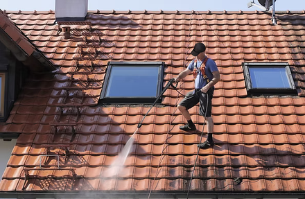 Worker pressure-washing a red tiled roof beside two skylights