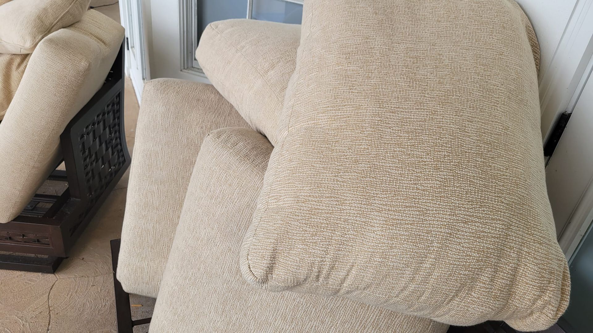 Pile of light tan textured outdoor cushions next to a matching couch.