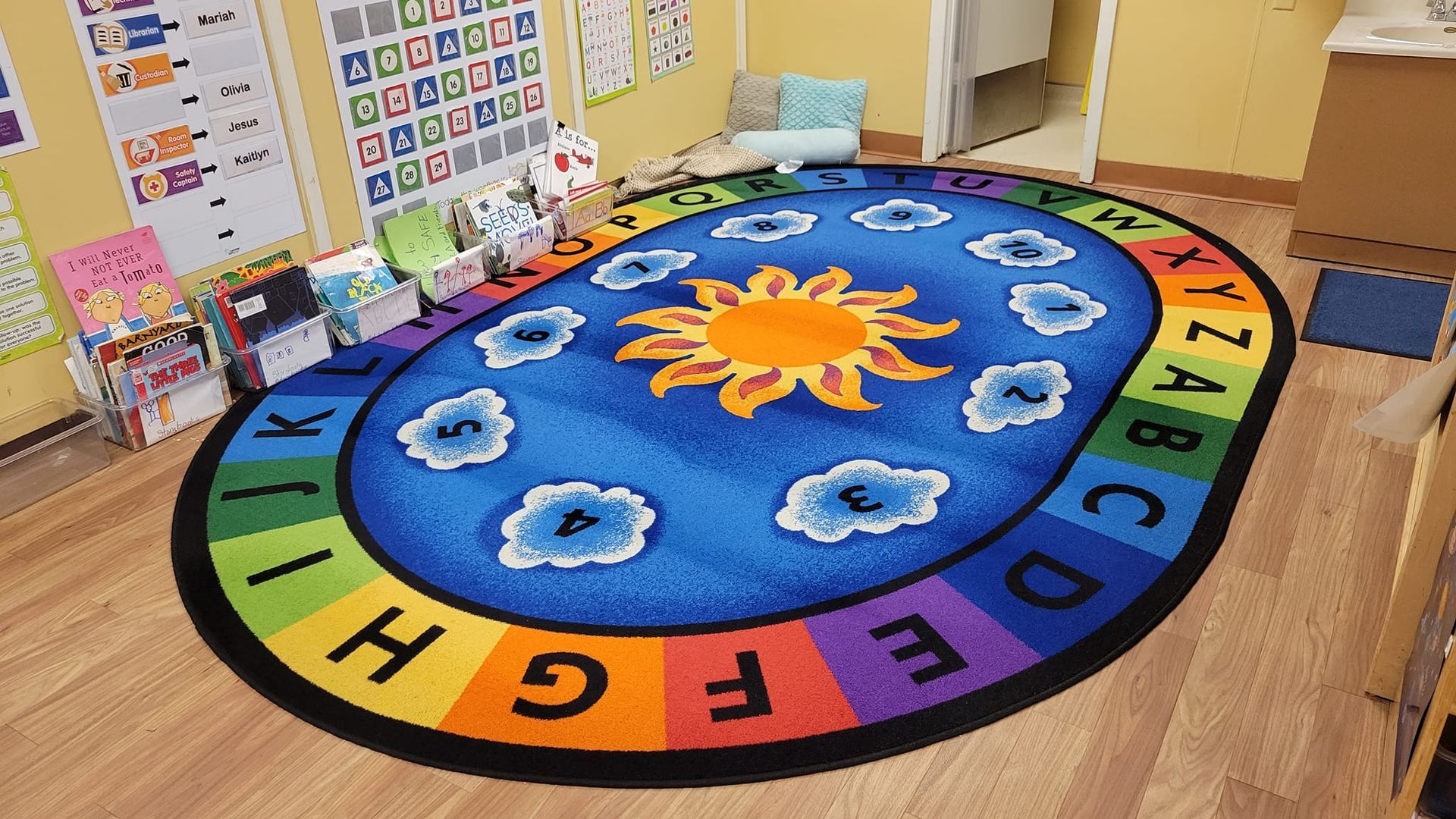 Classroom with alphabet rug and sun design. Rainbow letters, clouds, books, and storage shelves.