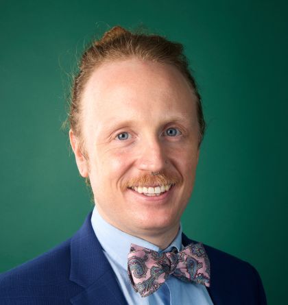 Portrait of a smiling man in a blue suit and floral bow tie against a green background