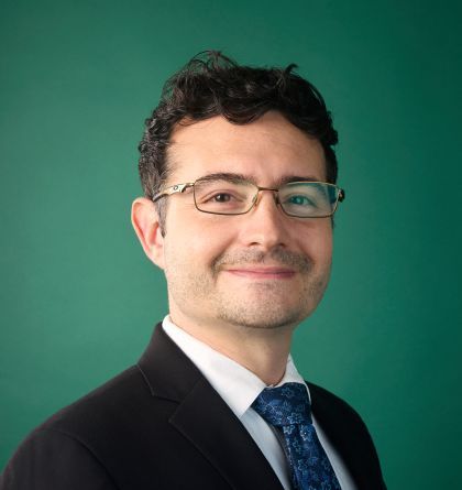 Portrait of a smiling person in a dark suit and blue tie against a green background