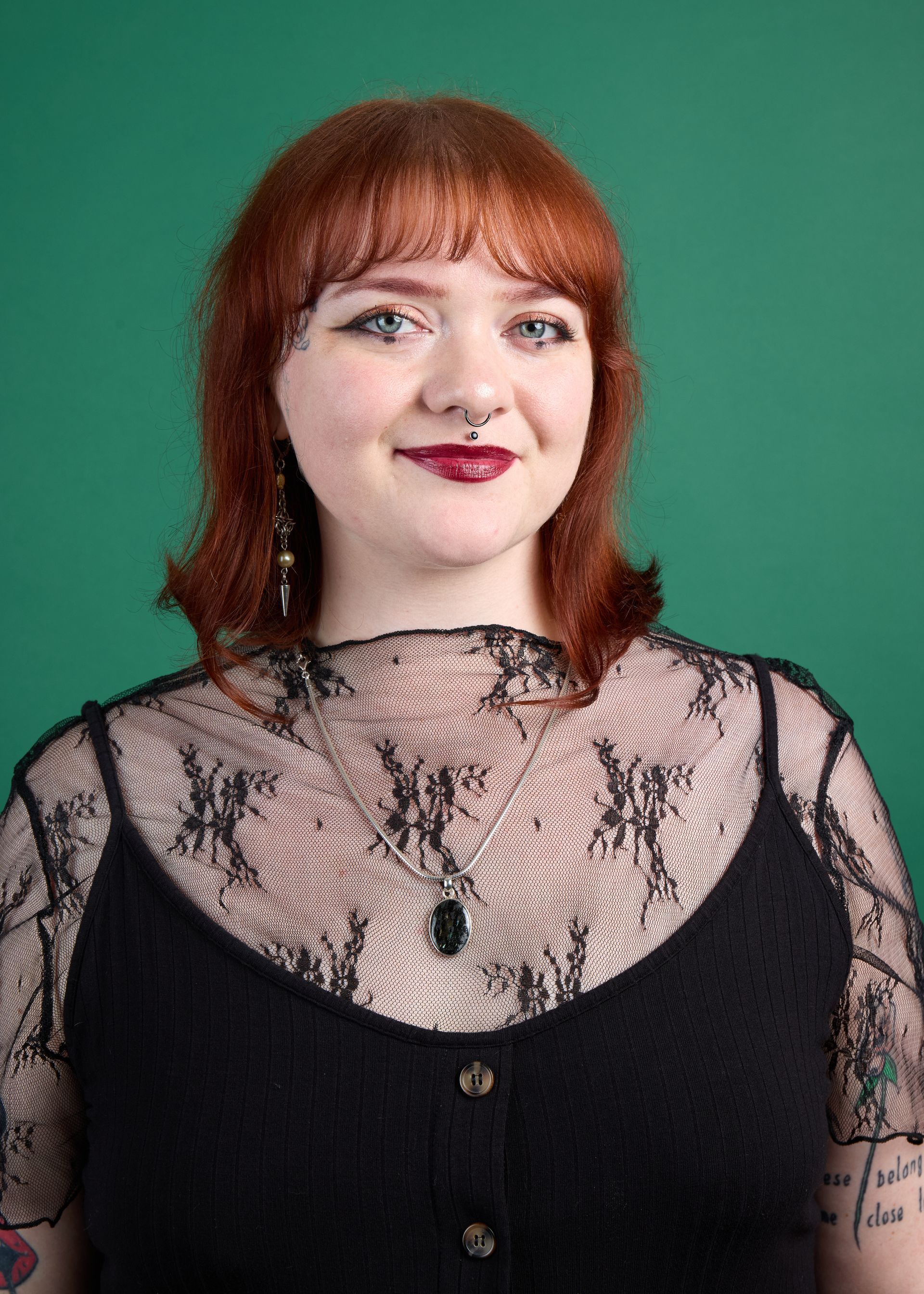 Portrait of a red-haired person in a black lace top against a green background