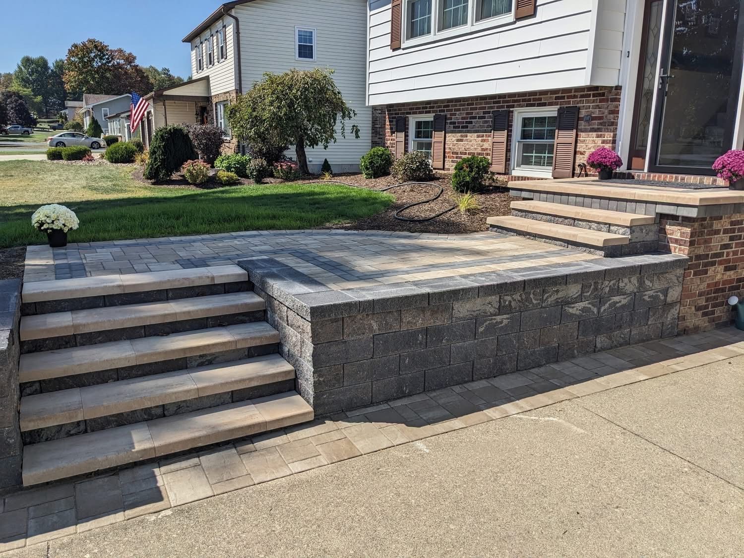 A house with a newly constructed patio and steps. Gray and tan pavers, brick facade, and landscaping are visible.