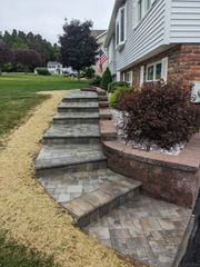 Stone steps leading up to a house with a brick facade and landscaping, featuring a small American flag.