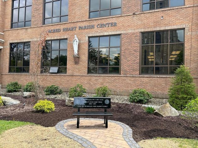 Exterior of a brick building with a bench in front. The building has large windows and a statue.