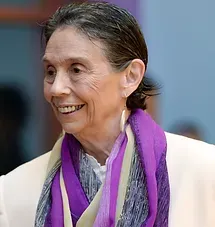 Smiling person in a white jacket and purple scarf against a blue background