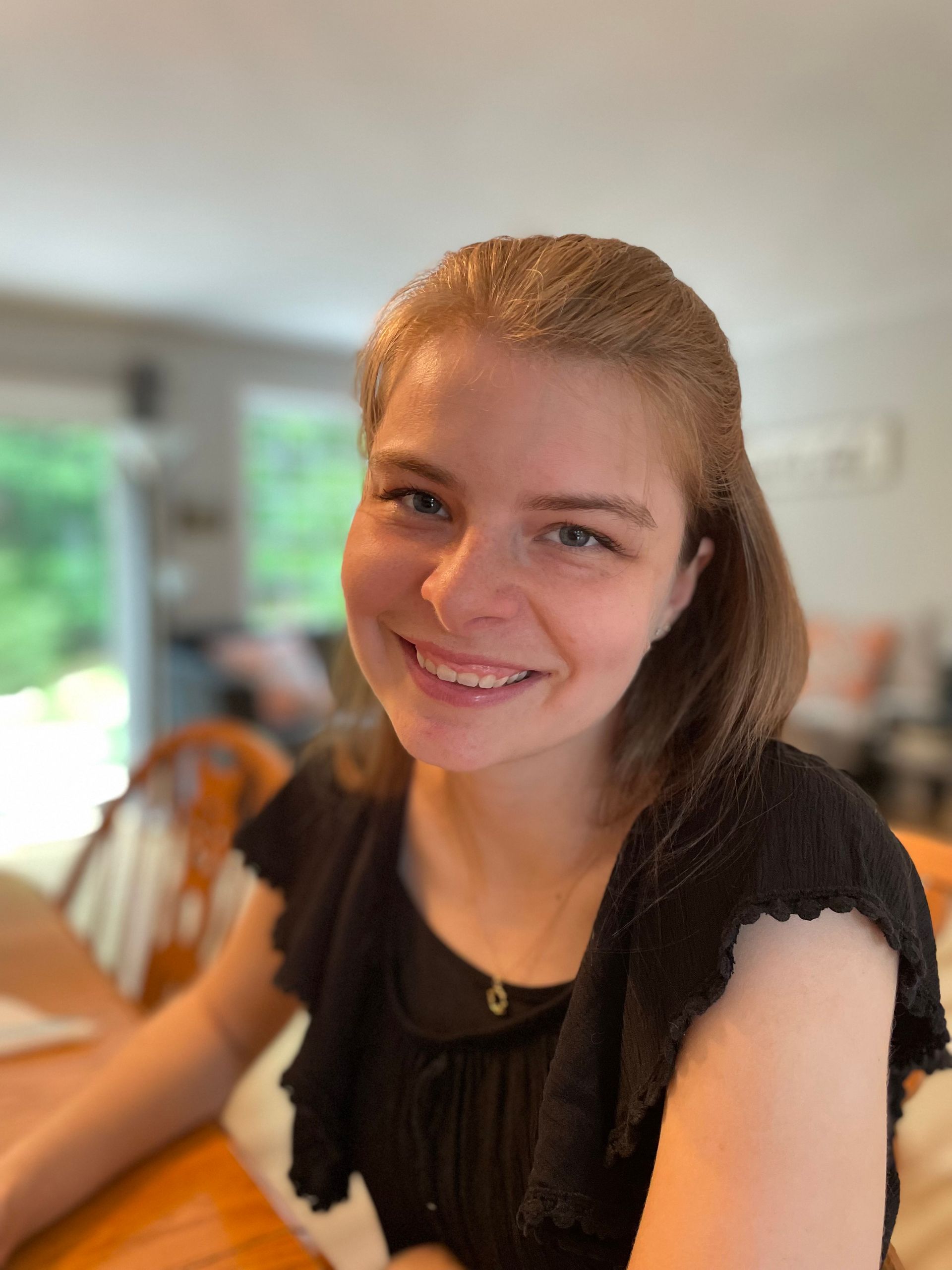 Smiling woman in a black top sitting indoors at a table, with a softly blurred background.