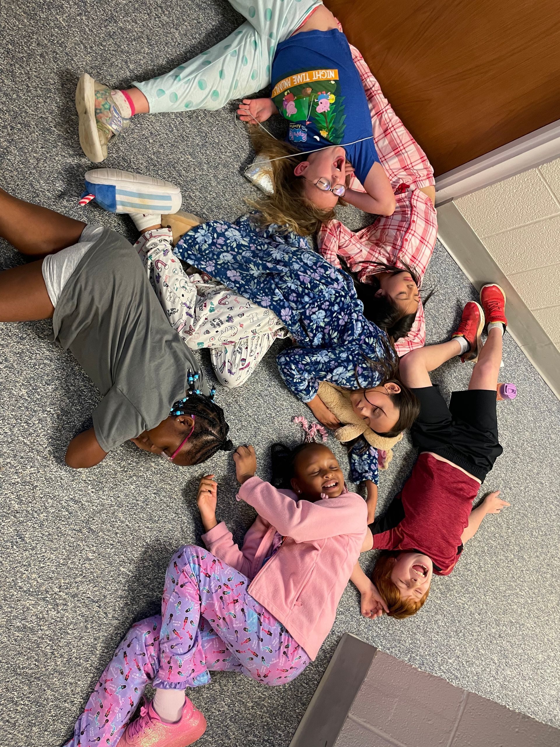 Children lying in a circle on the floor, touching feet, in colorful clothes.