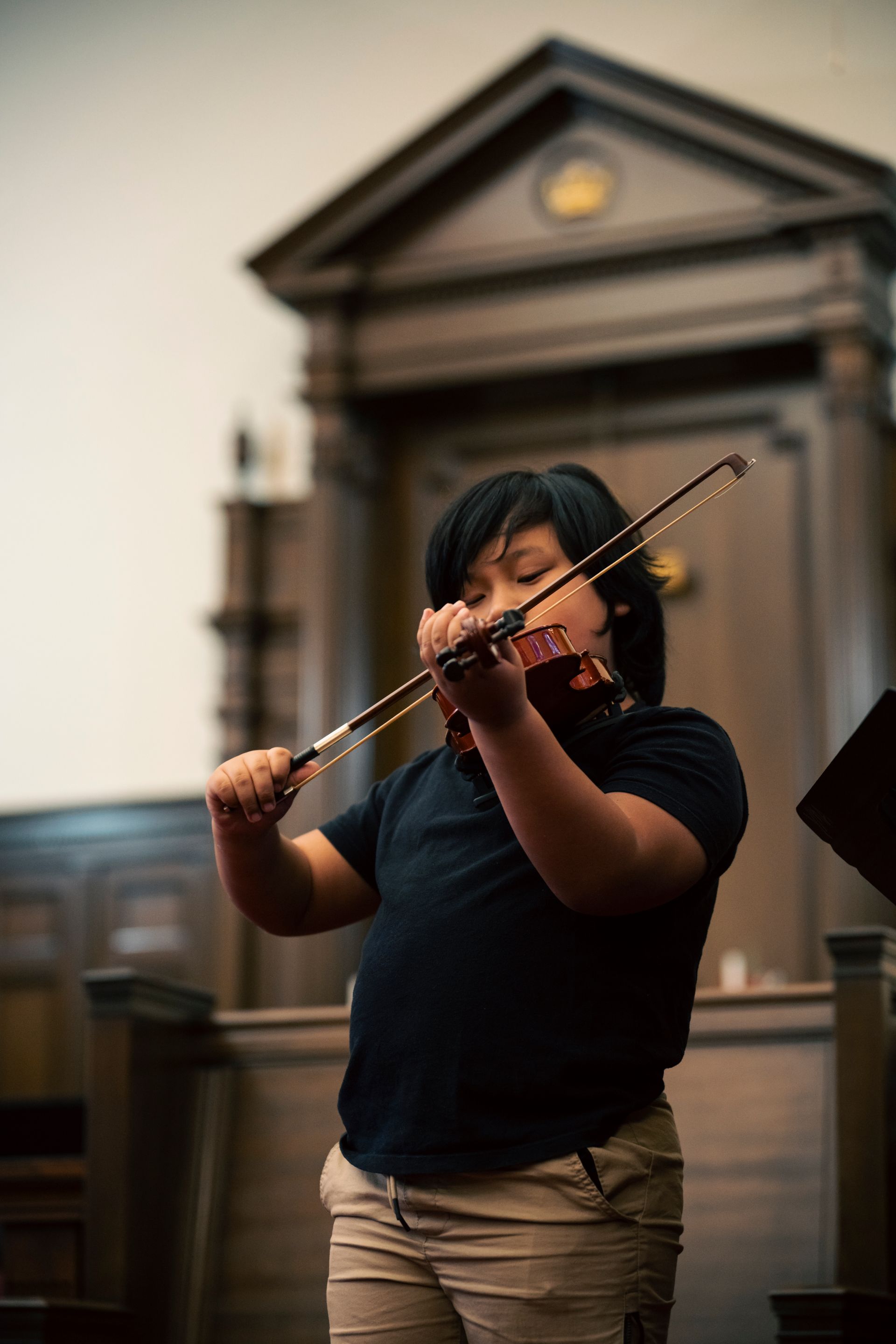 Person playing a violin indoors in front of a blurred classical building backdrop